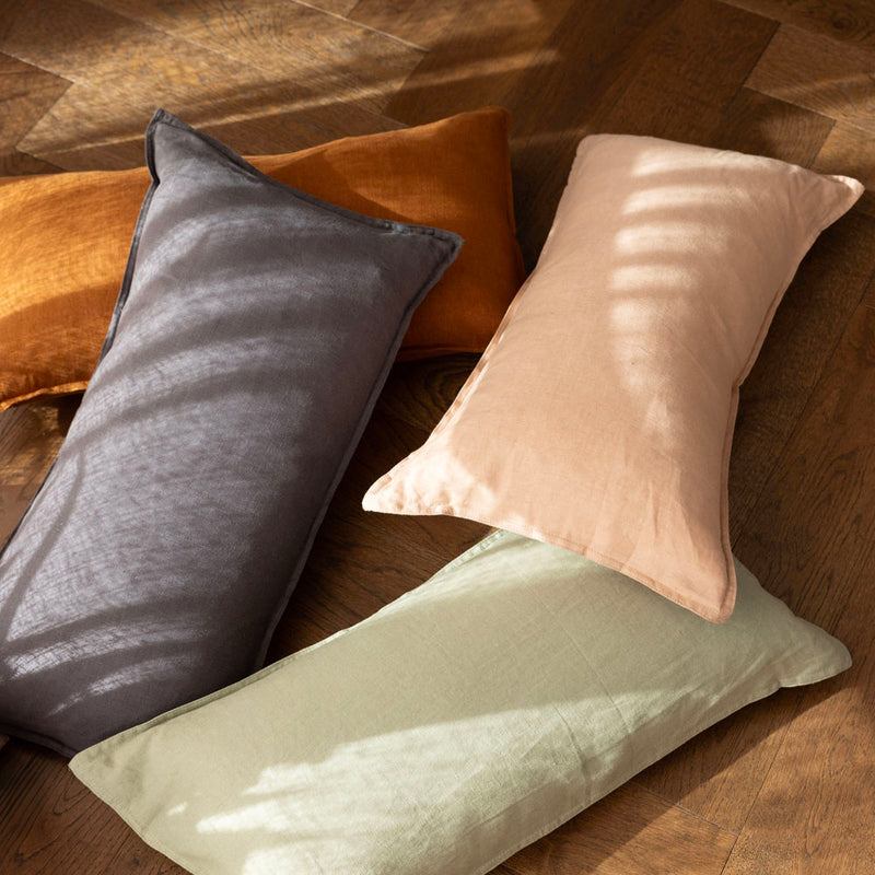 Bambury's Linen Rectangle Cushions in Charcoal, Sage, Hazel & Tea Rose, scattered on a wooden floor.